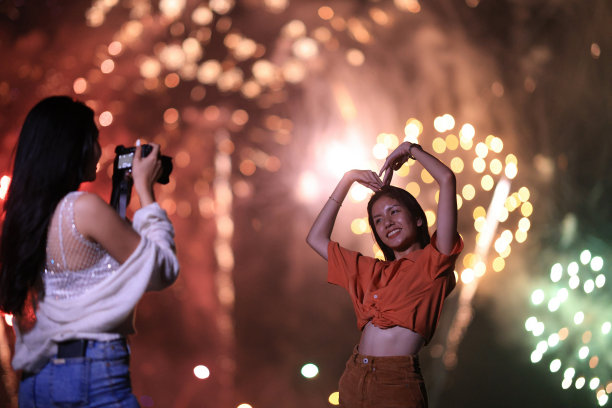 亲密的朋友用智能手机在巨大的烟花庆祝活动中拍照，快乐的年轻女子庆祝除夕图片下载