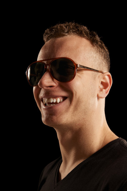 肖像的快乐的年轻人在时尚的太阳镜摆姿势，微笑孤立在黑色的工作室背景。时尚和生活方式的概念图片下载