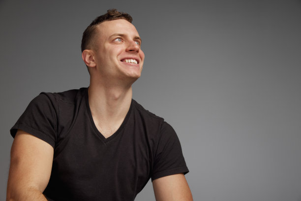 肖像的年轻人摆着棕色t恤，休闲服装孤立在灰色的工作室背景。愉快地微笑着。时尚和生活方式的概念图片下载