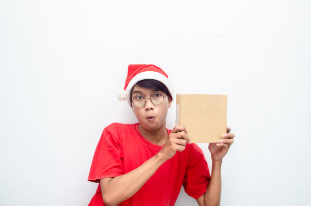 快乐迷人的亚洲男子在红色圣诞主题拿着纸盒礼物。图片下载