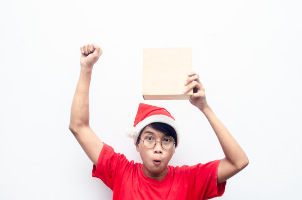 快乐迷人的亚洲男子在红色圣诞主题拿着纸盒礼物。图片下载