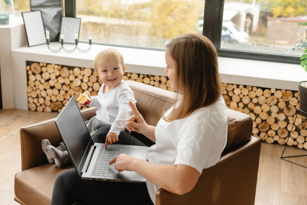 在家工作。母亲通过笔记本电脑远程工作，旁边的儿子妨碍了她的工作。图片下载