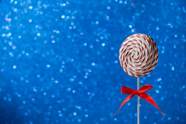 圆形的棒棒糖，红色和白色螺旋。硬糖焦糖，棒棒糖在闪闪发光的蓝色背景。圣诞节的概念图片下载