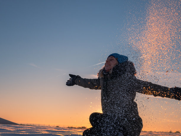 日落时分，一位妇女在美丽的雪原上向天空扔雪图片下载