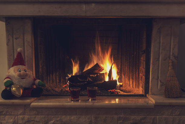 一个巨大的石头壁炉，燃烧的木头和两杯酒在圣诞节的晚上。图片下载