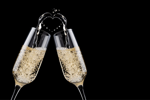 奢侈的金色流动的起泡香槟作为心脏与溅以上的酒杯在黑色背景，特写，细节，复制空间。爱浪漫的情人节背景与节日饮料为设计。图片下载