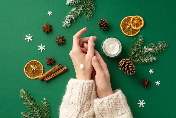 第一人称俯视图照片的妇女在她的手涂抹奶油罐松果干橙片肉桂棒茴香雪花和杉木枝在霜冻孤立的绿色背景图片下载