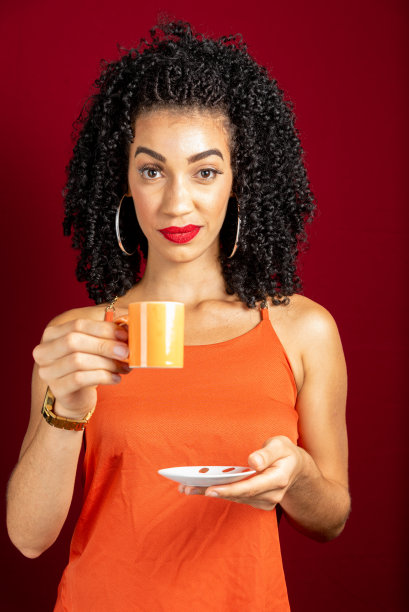 画像年轻美丽的女人，拿着一杯咖啡，穿着橙色的衣服。图片下载