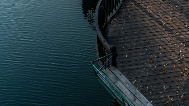 湖面上的木地板被阳光照亮，覆盖着秋叶，有铁栅栏图片下载