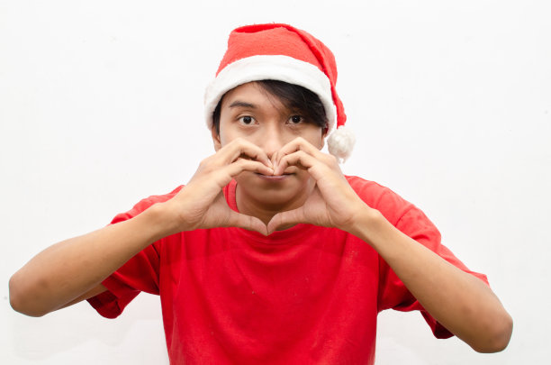 富有表现力的快乐自信的年轻亚洲人在圣诞老人主题的衣服给爱的手势图片下载