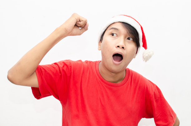 富有表现力的快乐亚洲年轻男子穿着圣诞老人主题的衣服，脸上带着震惊、惊讶和惊讶的表情。图片下载