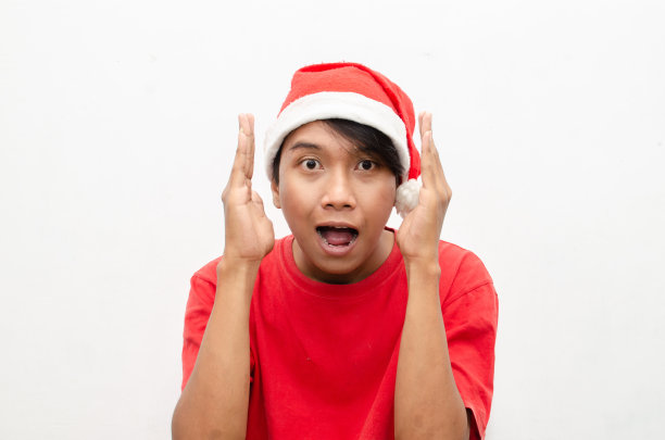 富有表现力的快乐亚洲年轻男子穿着圣诞老人主题的衣服，脸上带着震惊、惊讶和惊讶的表情。图片下载