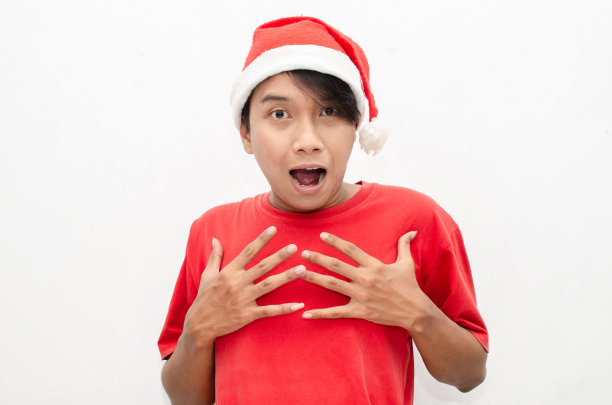富有表现力的快乐亚洲年轻男子穿着圣诞老人主题的衣服，脸上带着震惊、惊讶和惊讶的表情。图片下载