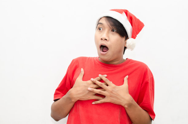 富有表现力的快乐亚洲年轻男子穿着圣诞老人主题的衣服，脸上带着震惊、惊讶和惊讶的表情。图片下载