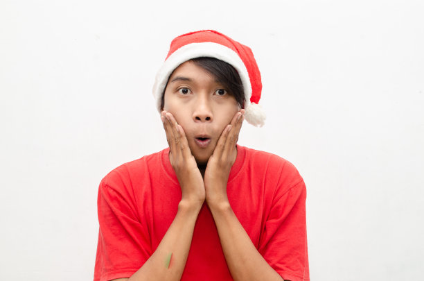 富有表现力的快乐亚洲年轻男子穿着圣诞老人主题的衣服，脸上带着震惊、惊讶和惊讶的表情。图片下载