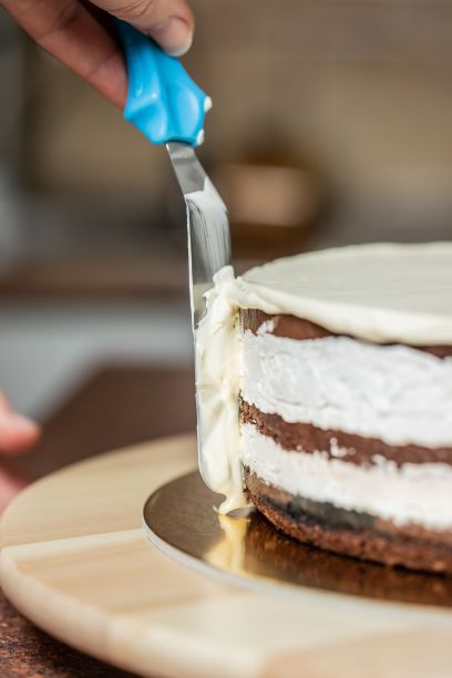 在厨房里，一个女人用抹刀在抹巧克力蛋糕的边缘图片下载