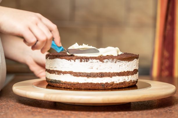 在厨房里，一个女人用抹刀把鲜奶油抹在刚烤好的巧克力蛋糕上图片下载