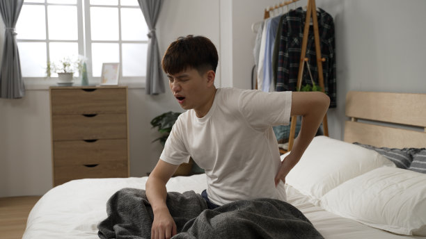 一名感到腰痛的亚洲日本男子早上在家里醒来后，一边按摩自己，一边痛苦地呻吟着图片下载