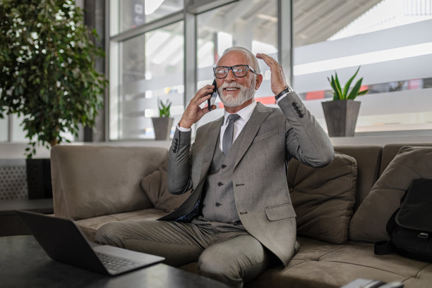 面带微笑的老年企业家在商务办公室里一边用笔记本电脑一边用智能手机讨论图片下载