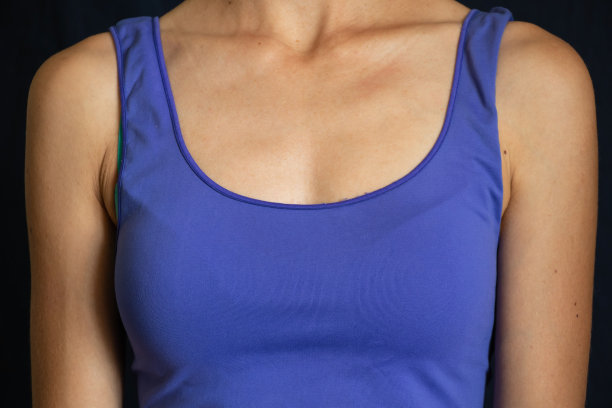 一个穿蓝色t恤的女孩的胸部，深色背景特写图片下载