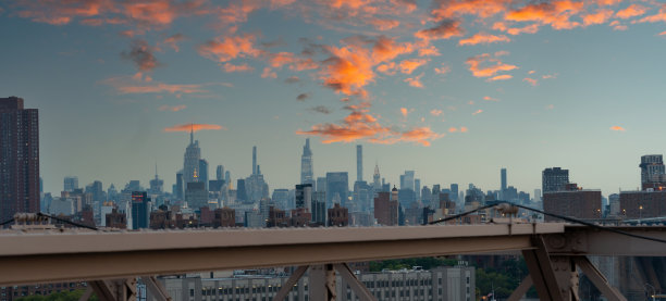 从布鲁克林大桥上俯瞰日落时分曼哈顿下城的摩天大楼全景，天空绚丽多彩图片下载