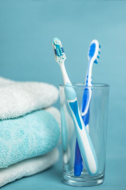 垂直拍摄玻璃杯里的两只蓝色牙刷，蓝色背景上有毛巾——健康概念图片下载
