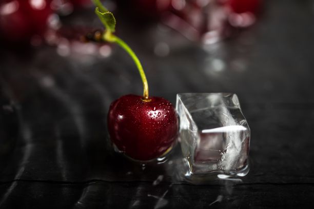 特写一个红色的新鲜樱桃和一个冰块在黑色的桌子背景图片下载