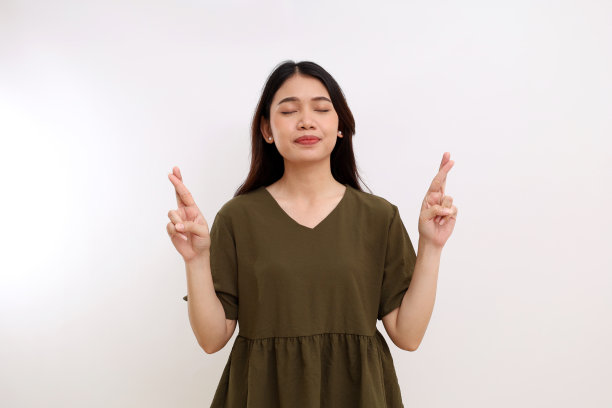 年轻的亚洲妇女站着交叉手指或希望的手势和闭上眼睛。孤立在白色背景中图片下载