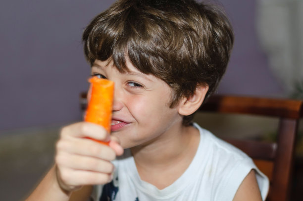 快乐的小男孩吃着新鲜的胡萝卜，玩得很开心。图片下载