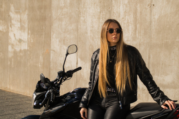 漂亮的白人女士穿着皮夹克和全黑的衣服，旁边是她的摩托车图片下载