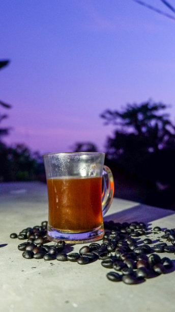 一杯黑咖啡，用玻璃杯盛着，周围撒着一些烤过的咖啡豆图片下载