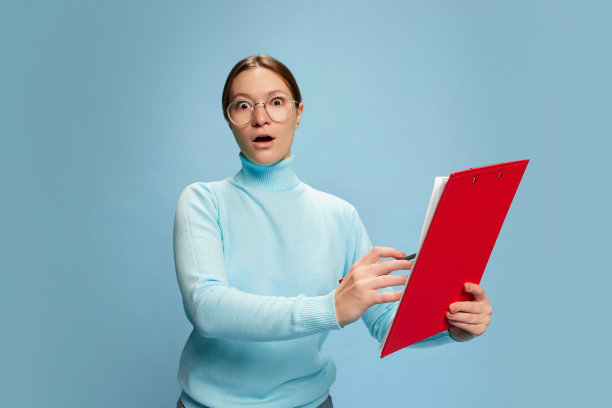 年轻女子的肖像与震惊的脸看通过文件隔离在蓝色背景。职业、教育观念图片下载