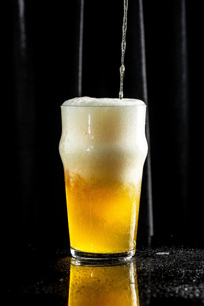 深色背景下的一杯啤酒。啤酒被倒进玻璃杯里图片下载