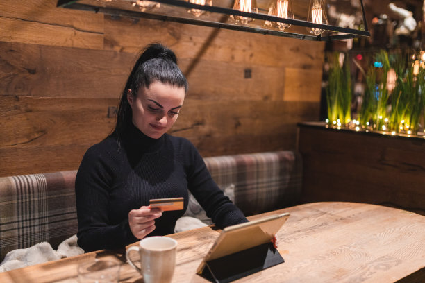 坐在咖啡馆里拿着信用卡并使用平板电脑的漂亮年轻女人图片下载