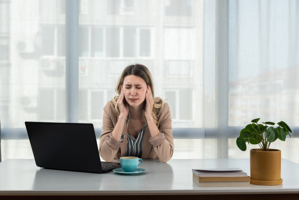 疲惫不安的年轻商业女性坐在桌上的笔记本电脑，靠在手上的头，遭受头痛，感到沮丧，不快乐，疲劳，得到坏消息。职业倦怠概念图片下载