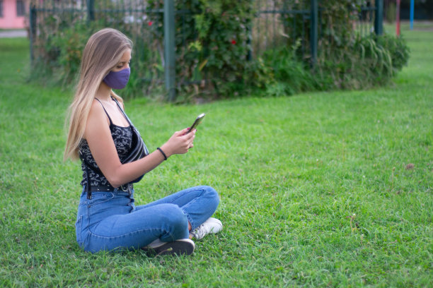 一个白人模特坐在草地上盯着手机的美丽照片图片下载