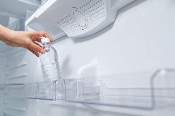 年轻女子从冰箱的架子上拿出一瓶水的短镜头图片下载