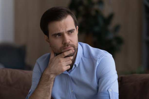 不快乐的年轻商人揉着下巴，看向别处，思考问题图片下载