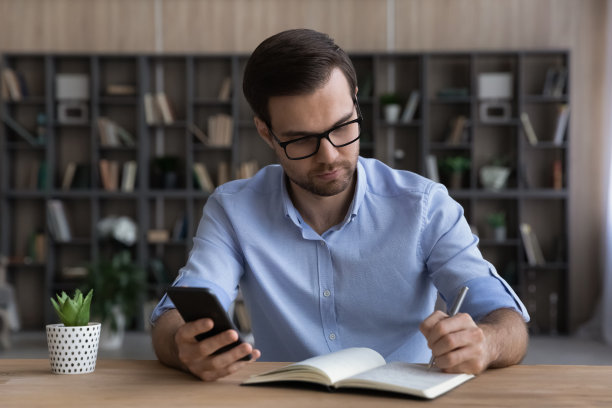 千禧一代的男经理戴着眼镜，用手机手写业务计划图片下载