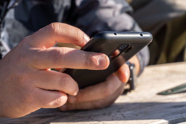 阳光明媚的户外，男性的手触摸着手机屏幕图片下载