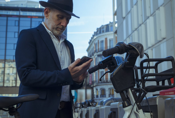 穿着西装和帽子的成年男子在街上用手机租用电动自行车。马德里,西班牙图片下载