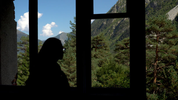 从一幢废弃建筑的窗户望出去的青山。一位年轻女子走到窗前。图片下载