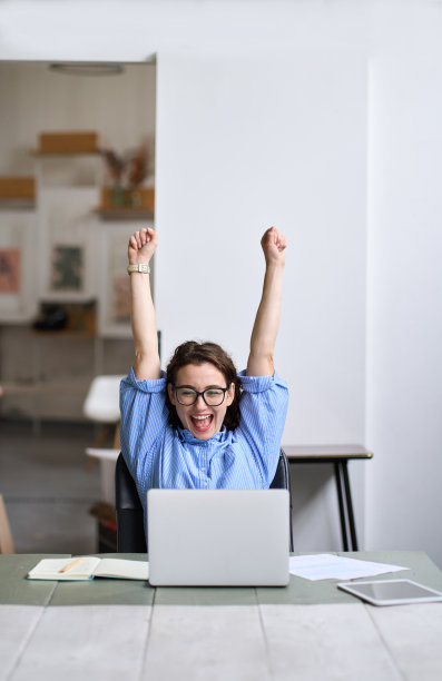 年轻快乐的女学生举手获胜在线看着笔记本电脑。图片下载
