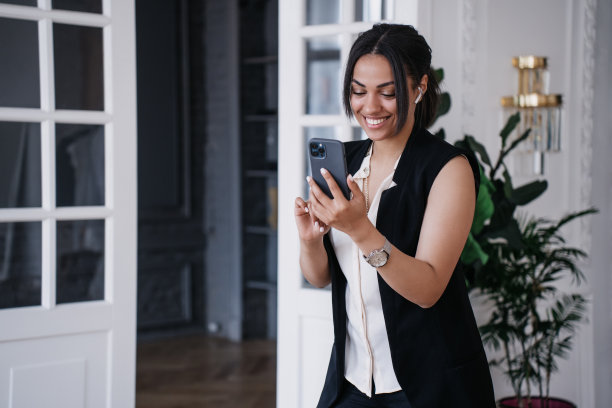漂亮的年轻巴西企业家使用电话和耳机通过互联网通话，在家远程工作的女性。快乐的非裔美国女士阅读来自父母的信息。图片下载