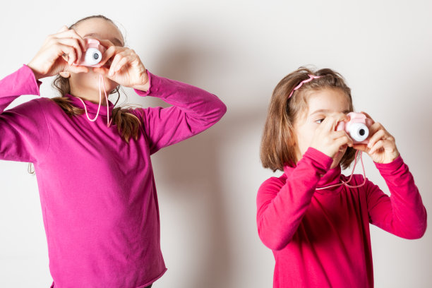 两个小女孩用白色背景的玩具相机拍照图片下载