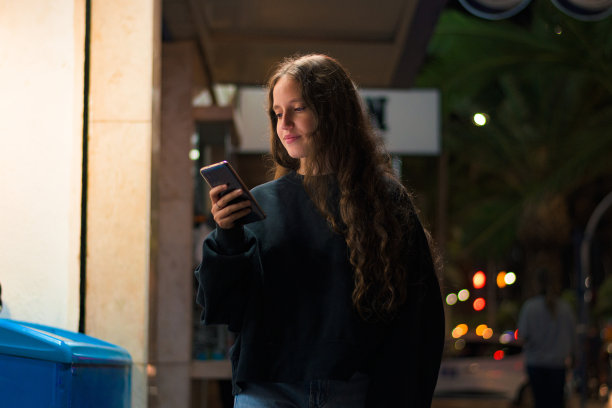 年轻女子带着手机走在夜里的街上图片下载