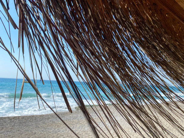 在温暖的东部热带国家南部天堂度假村的海滩上，透过黄色干燥的稻草遮阳伞，可以看到蓝色的海水和咸咸的海水。背景图片下载