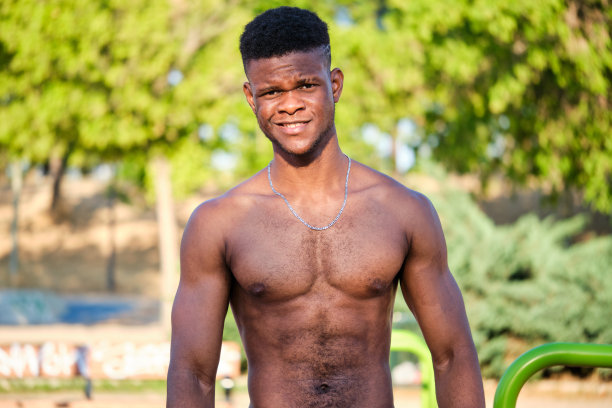 一个年轻健美的赤膊黑人男子在公园里微笑着看着相机的肖像。图片下载