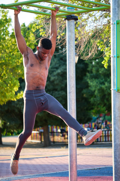 阳光明媚的日子，年轻健美的赤膊黑人男子在户外单杠上锻炼。图片下载