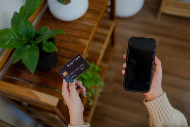 年轻的亚洲女子拿着信用卡，在家里用手机网购图片下载